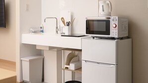 Una cocina compacta con microondas, tetera y un refrigerador pequeño.