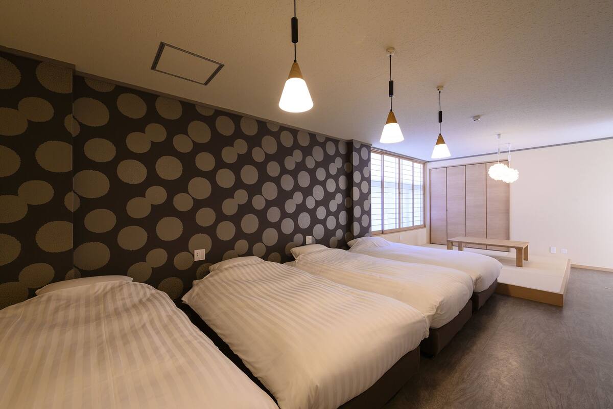A hotel room with three beds, a bench, a wardrobe, and a window with blinds.
