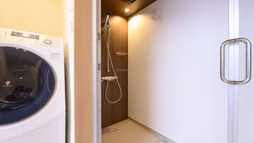 A compact bathroom with a washing machine, a shower, and a toilet.