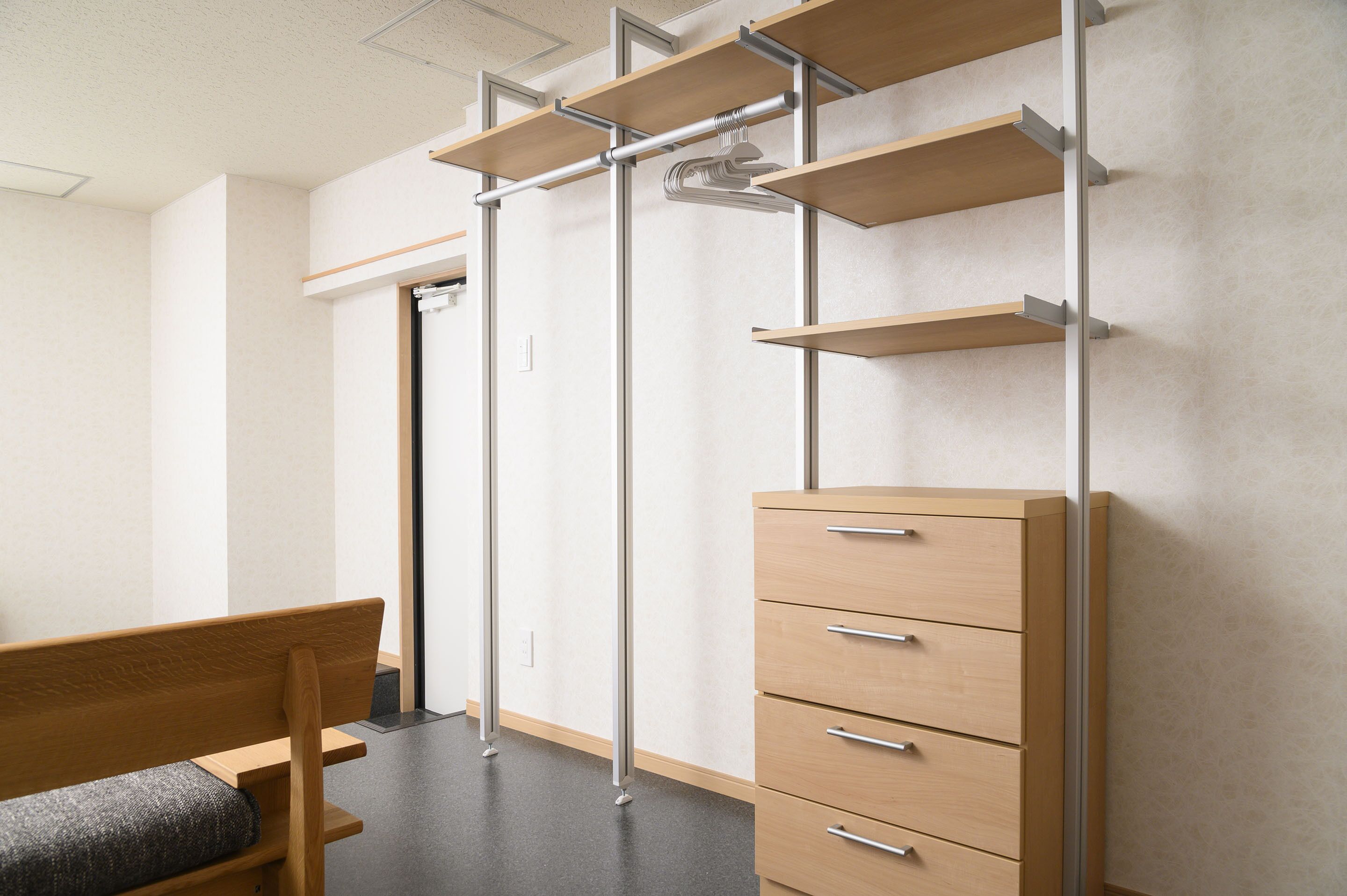 A room with a wooden bench, a cabinet with drawers, and a metal rack with shelves.