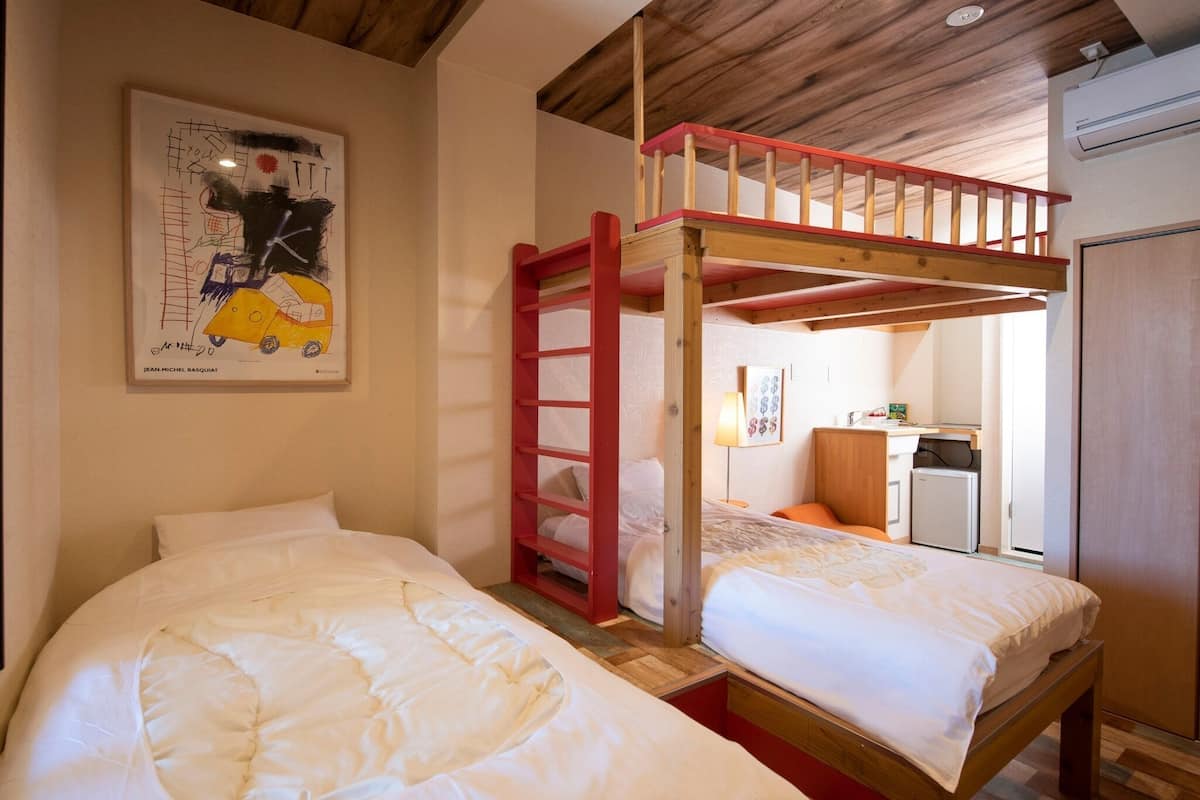 A room with two beds, a bunk bed, a wooden ceiling, and a wall-mounted artwork.