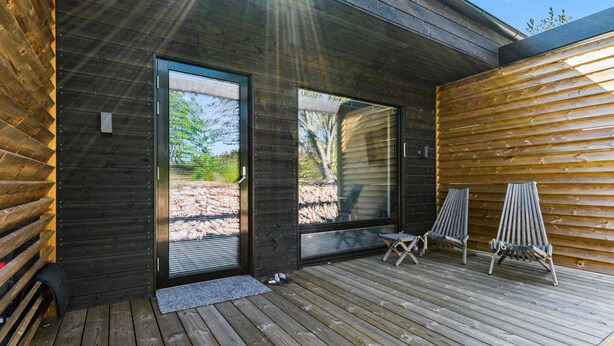 A modern wooden cabin with a deck, two chairs, and a small table.