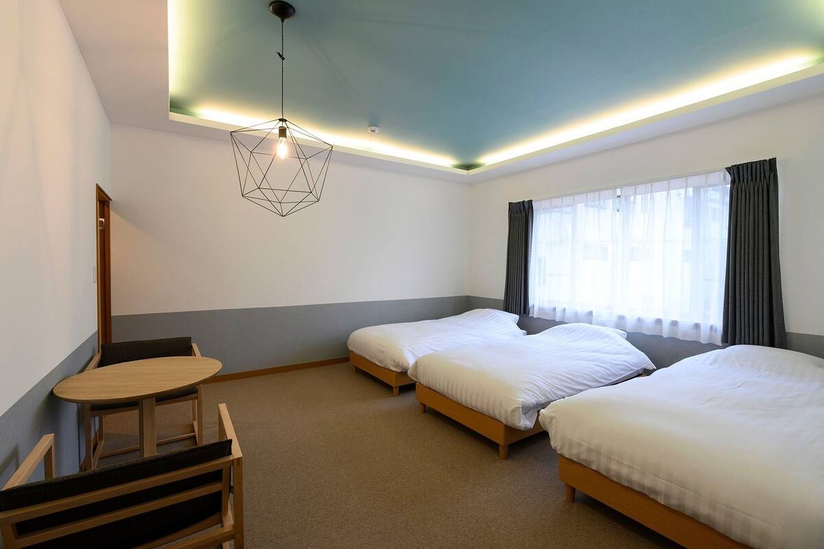 A hotel room with two single beds, a small wooden table, and a chair.