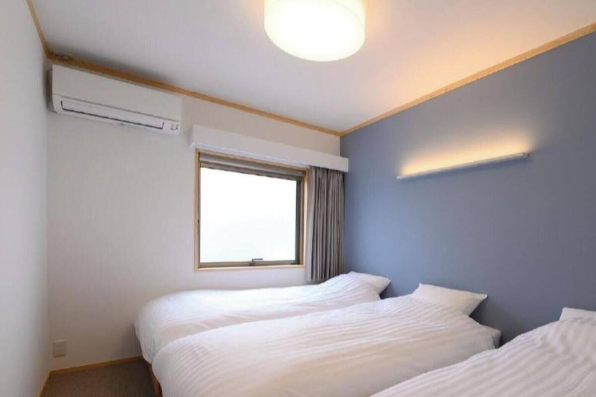 A hotel room with two beds, a window, and an air conditioning unit.