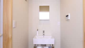 Un baño con lavamanos blanco, un espejo y un termostato fijado a la pared.