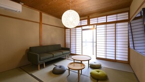 A traditional Japanese room with tatami flooring, a low green sofa, two tatami mats with cushions, a hanging light fixture, and shoji screens. - BEYOND HOTEL Takayama 4th (Takayama)