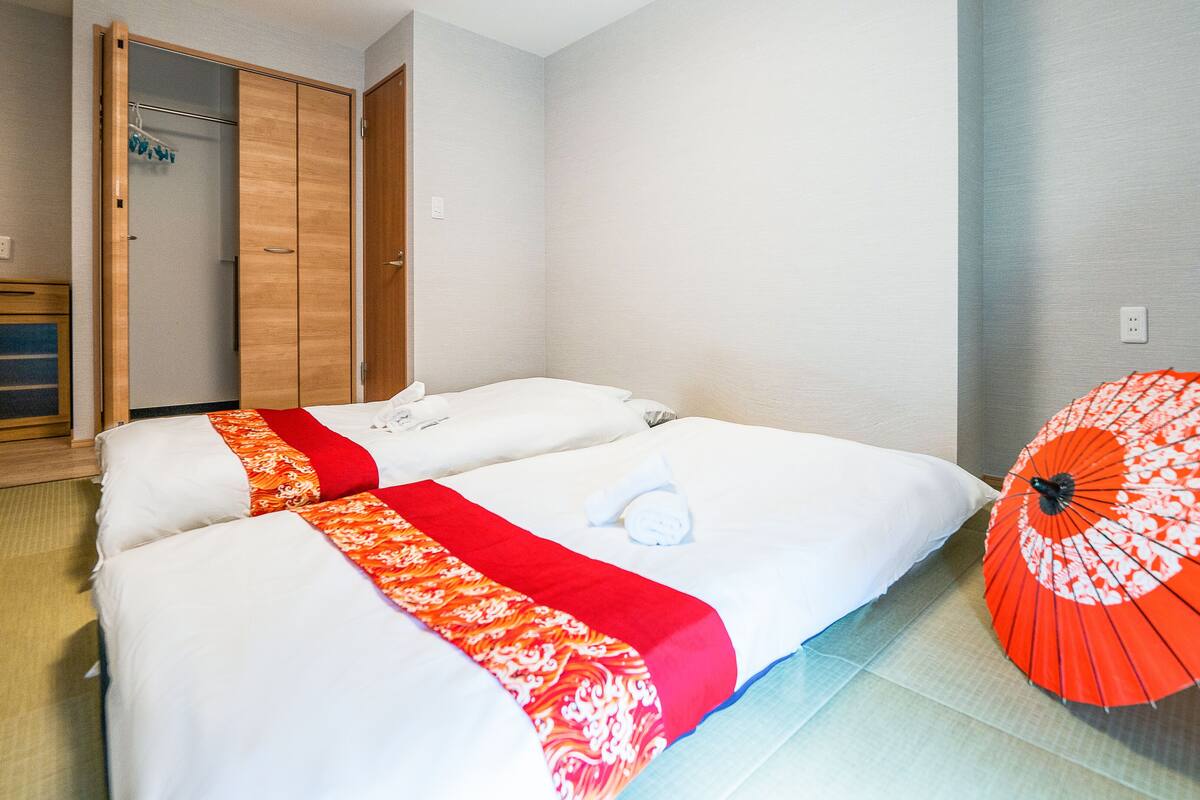 A hotel room with two beds, a wooden wardrobe, a bathroom, and a red umbrella.
