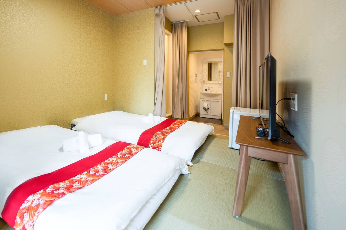 A hotel room with two beds, a desk, a television, and a bathroom visible through an open door.