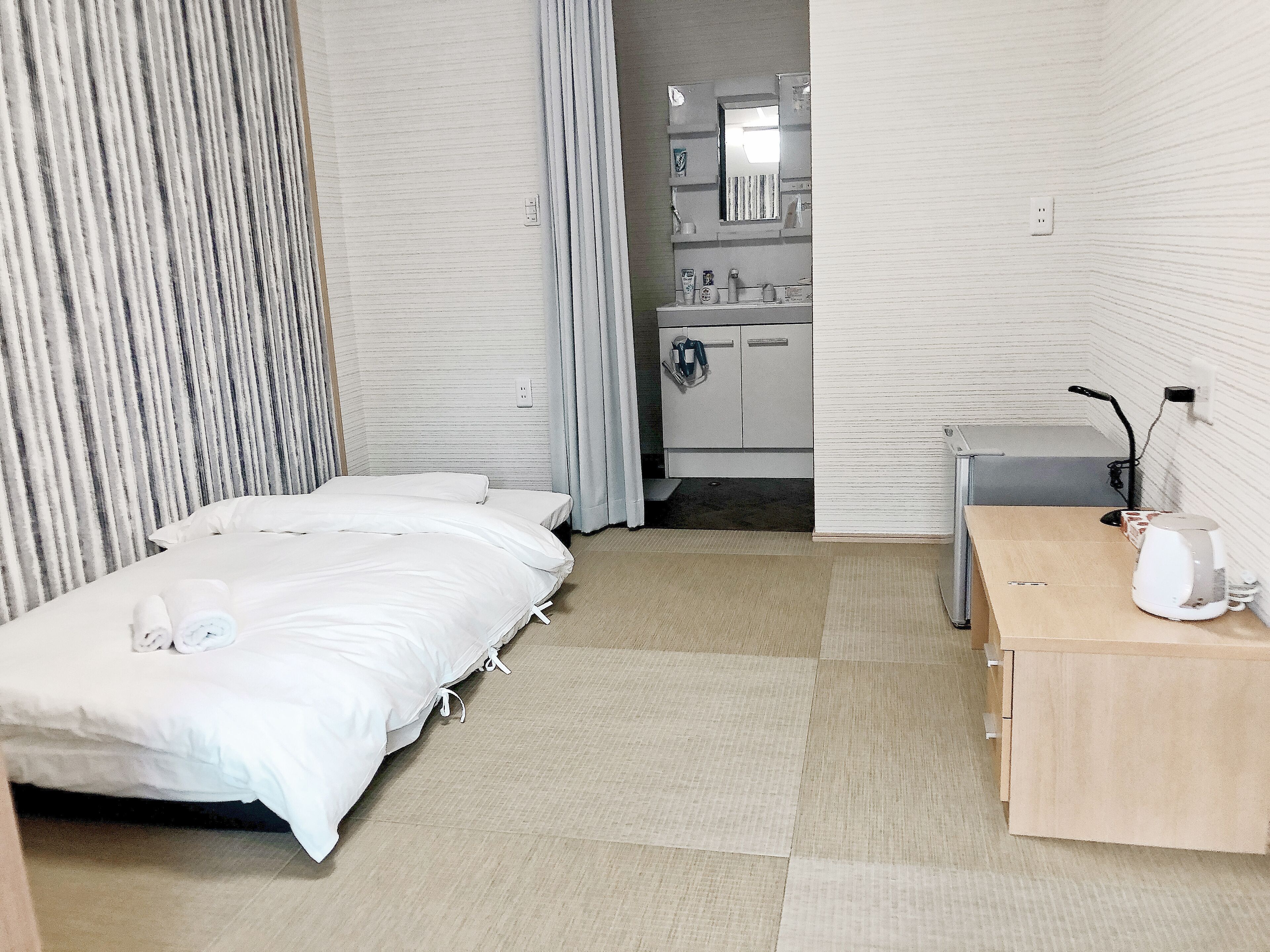 Ein Hotelzimmer mit Bett, kleinem Schreibtisch, Spiegel und einem durchgegangene Tür sichtbaren Badezimmer.