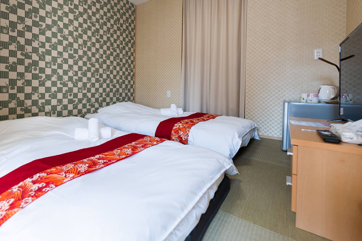 A hotel room with two beds, a desk, and a bathroom.