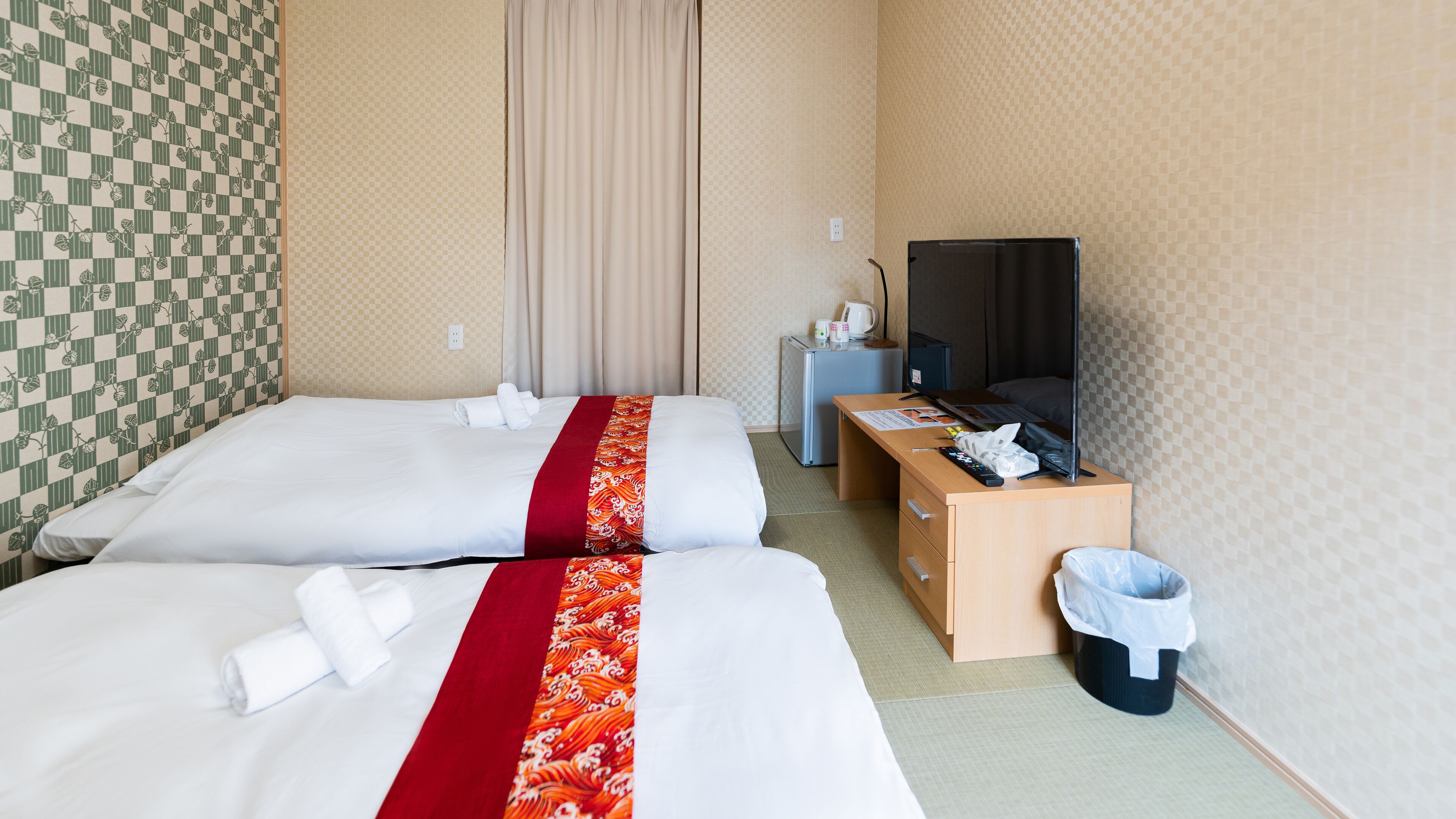 Ein Hotelzimmer mit zwei Betten, einem Schreibtisch, einem Fernseher und einem Mülleimer.