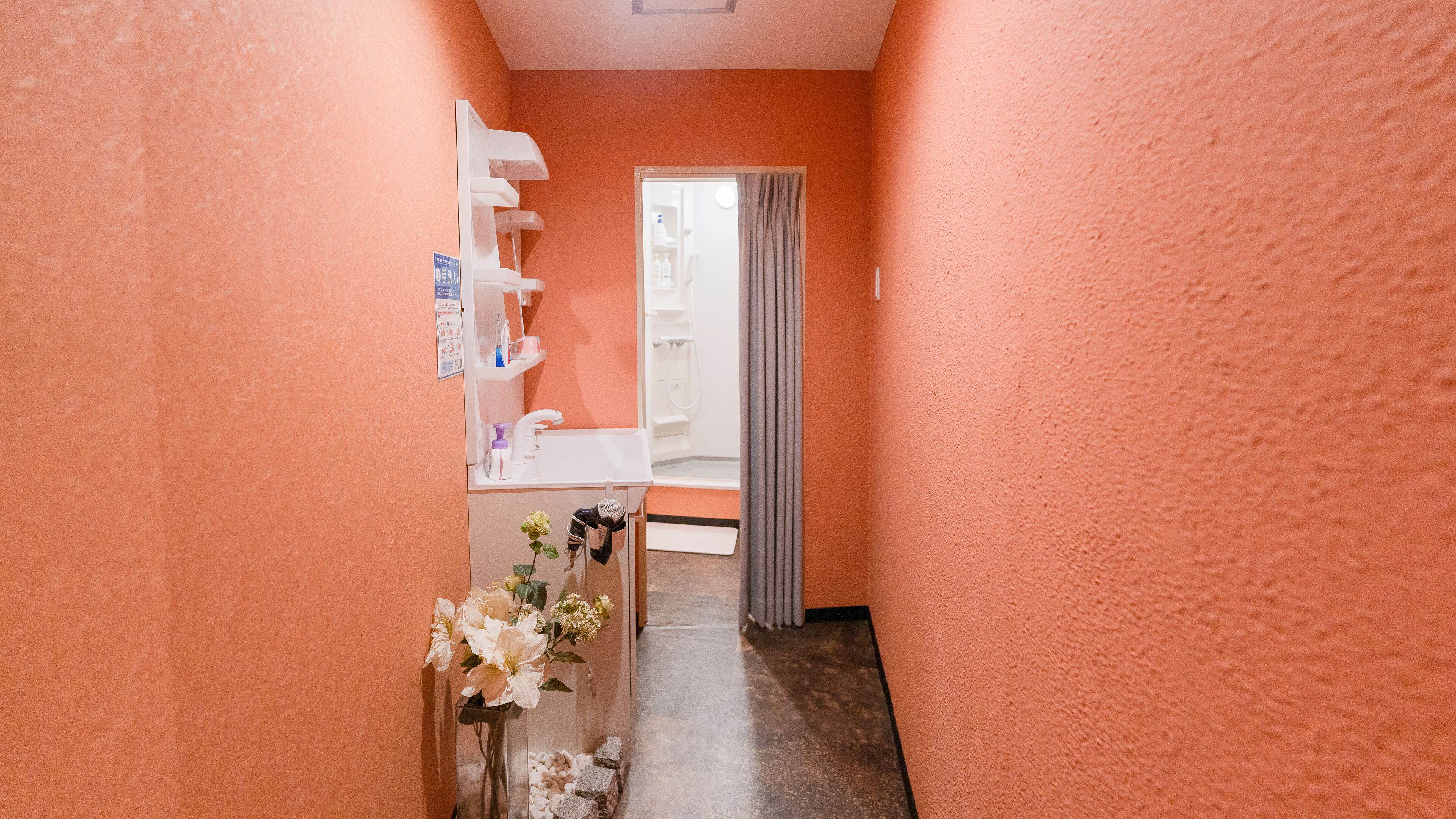 A hallway with a white sink, a mirror, and a vase with flowers.