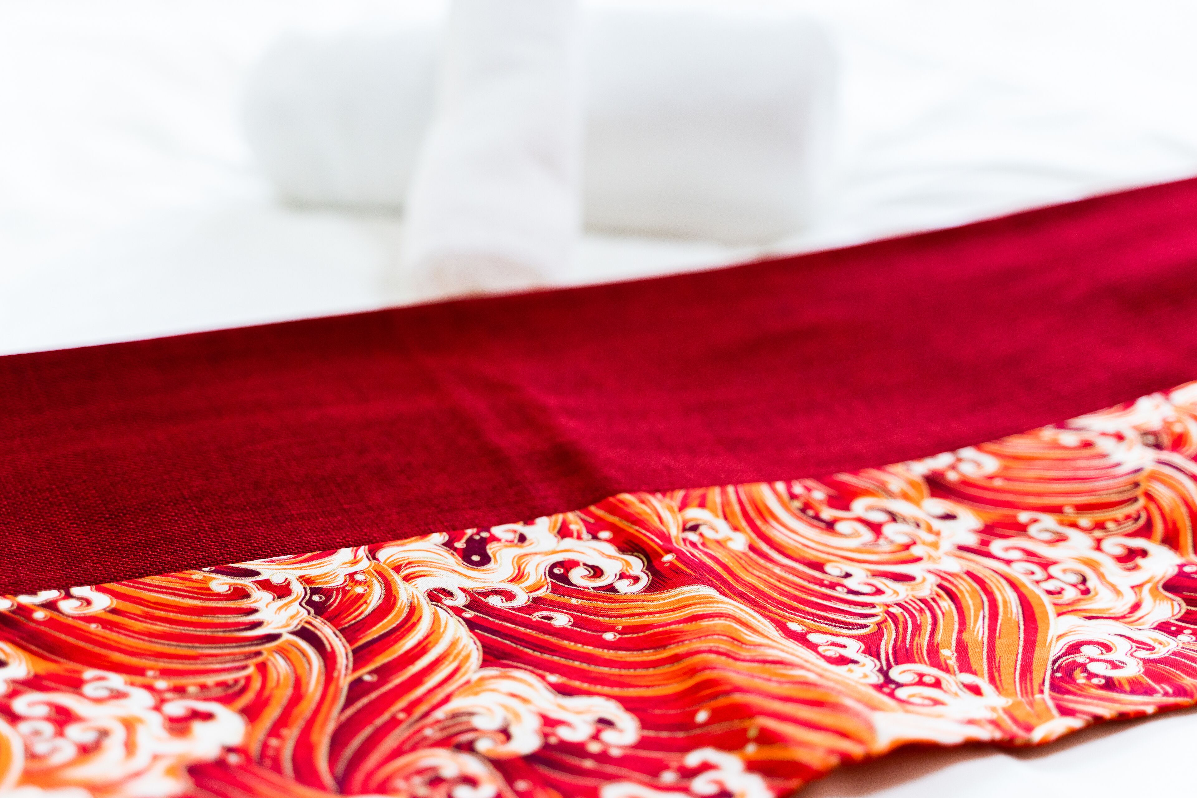 Una cama con sábana blanca y manta roja de estampado colorido.