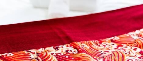Una cama con sábana blanca y manta roja de estampado colorido.