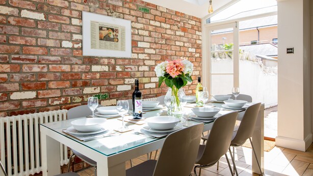 A dining area with a brick wall, a framed picture, a glass table, and chairs. - Stroll To The City Centre In From Chic Refurbished Townhouse (Cardiff)