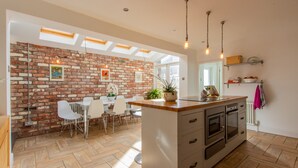 A modern kitchen with a brick wall, wooden flooring, and a central island with appliances. - Stroll To The City Centre In From Chic Refurbished Townhouse (Cardiff)