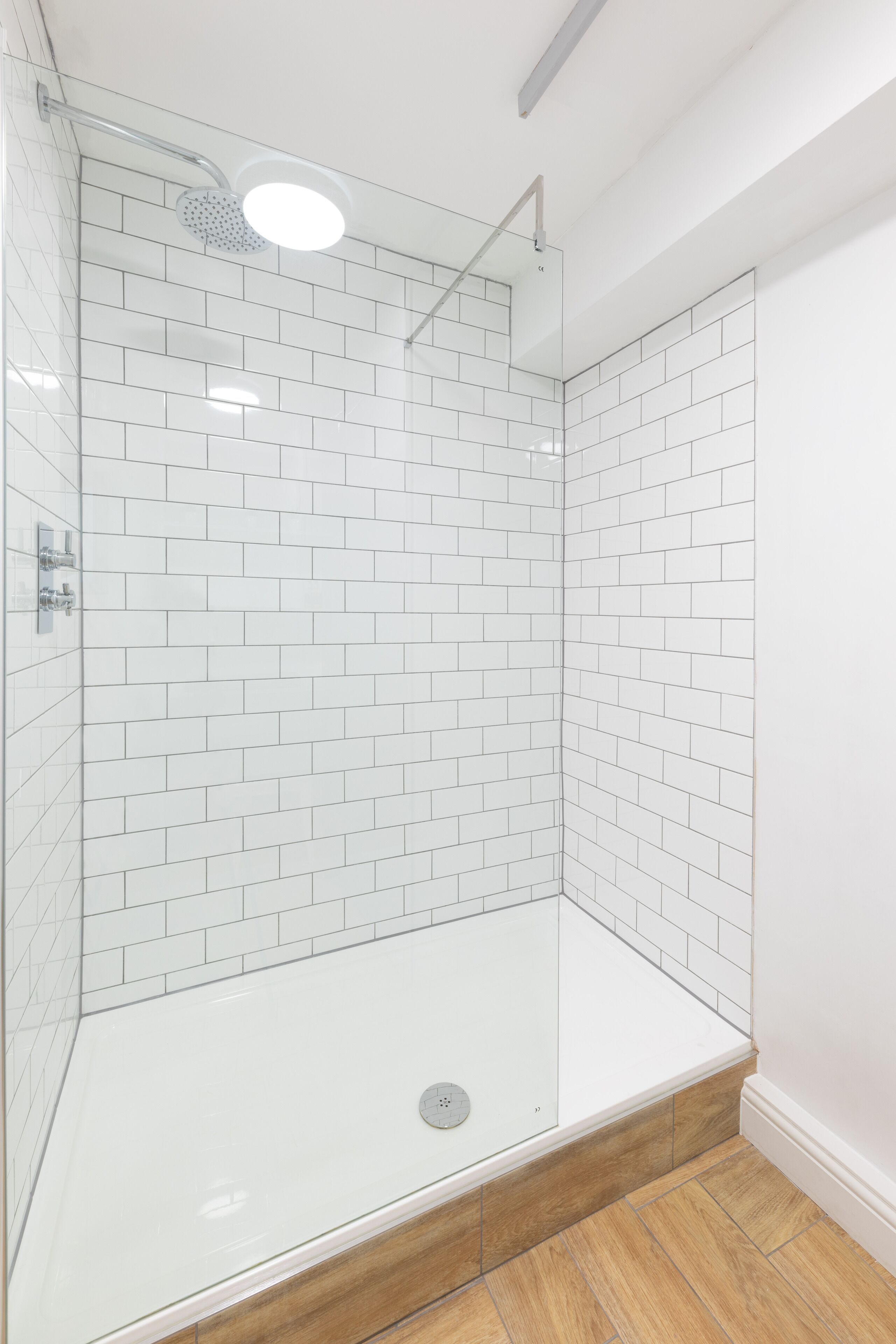 A modern shower with a glass enclosure, white tiled walls, and a wooden floor.