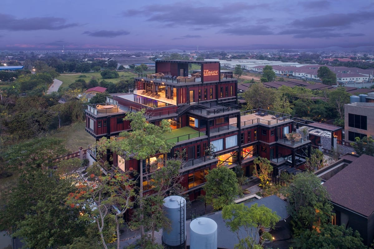 A multi-story building with a rooftop terrace, surrounded by greenery.