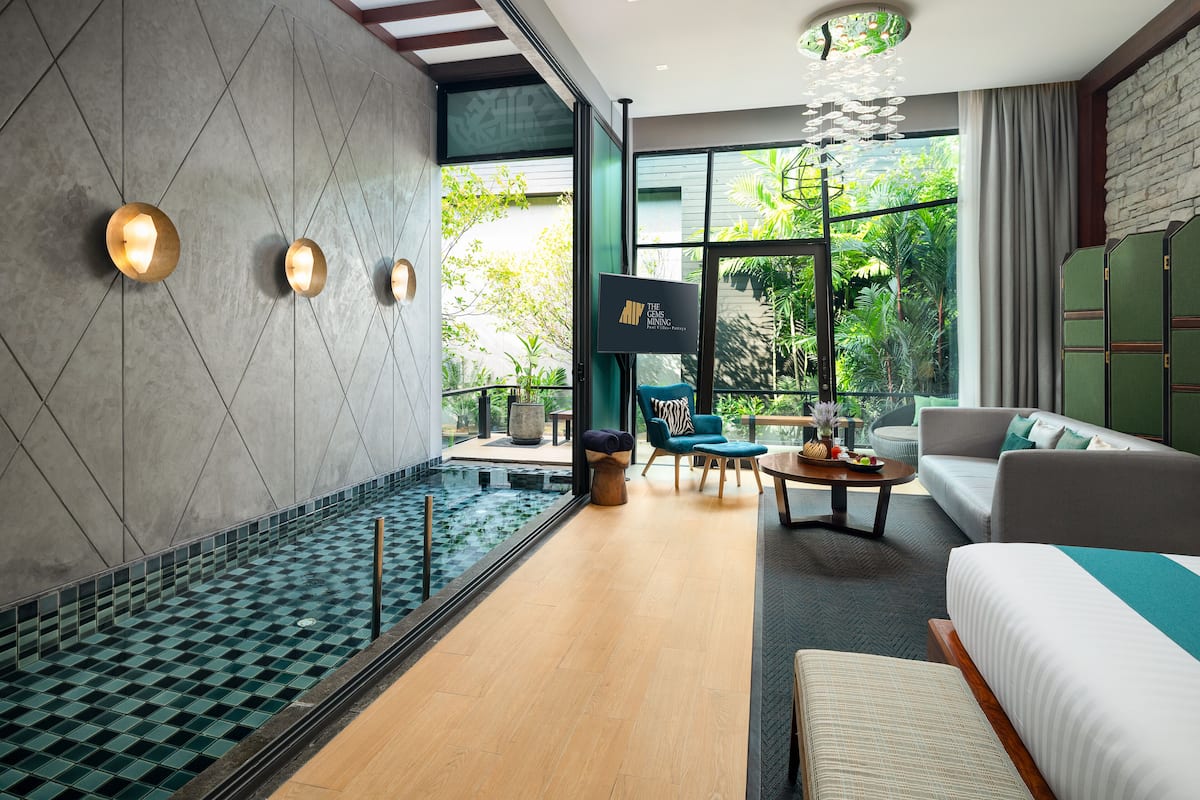 A modern hotel room with a large window, a small indoor pool, a sofa, and a TV.