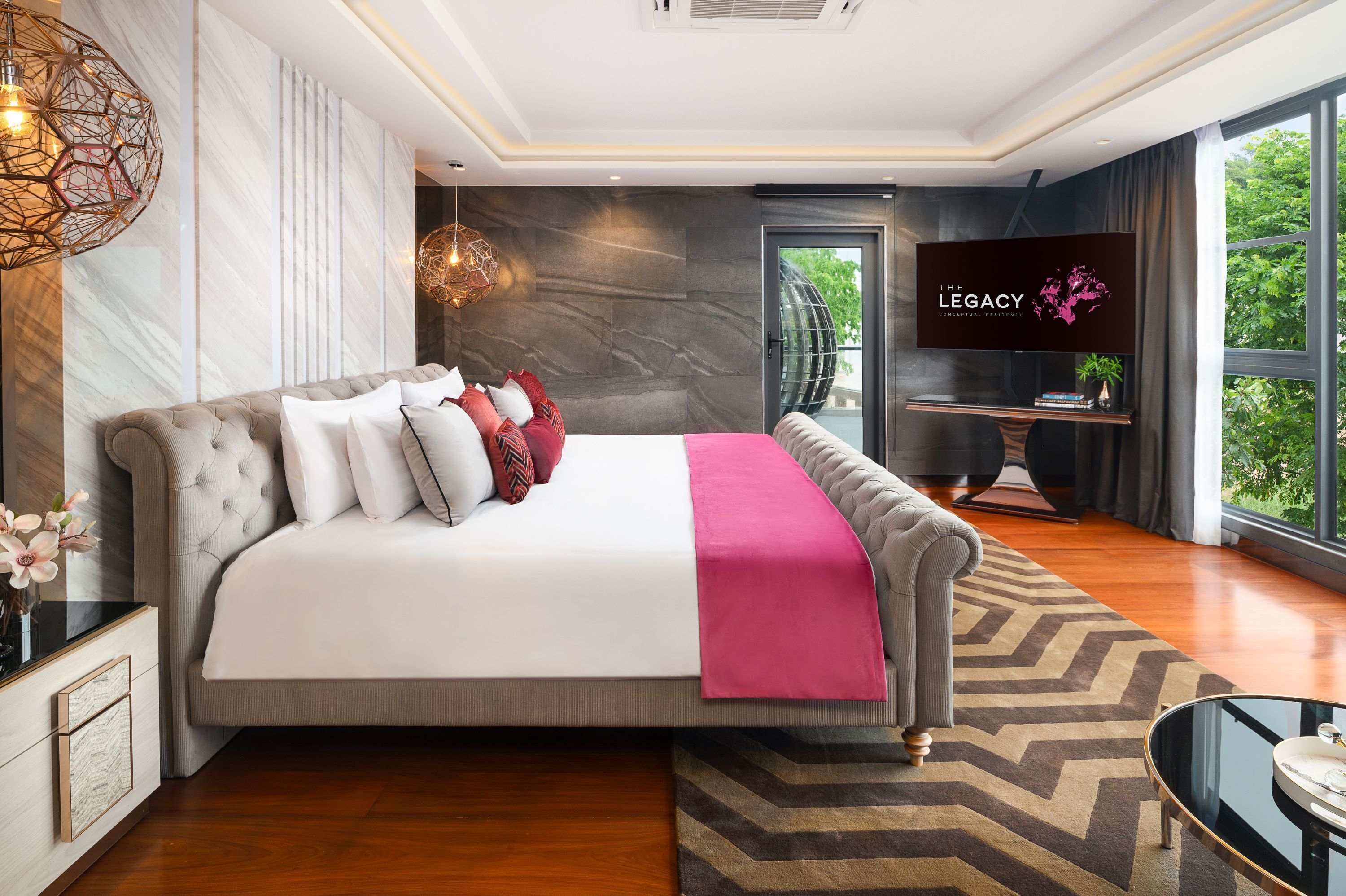 A modern hotel room with a large bed, a TV, and a view of greenery.