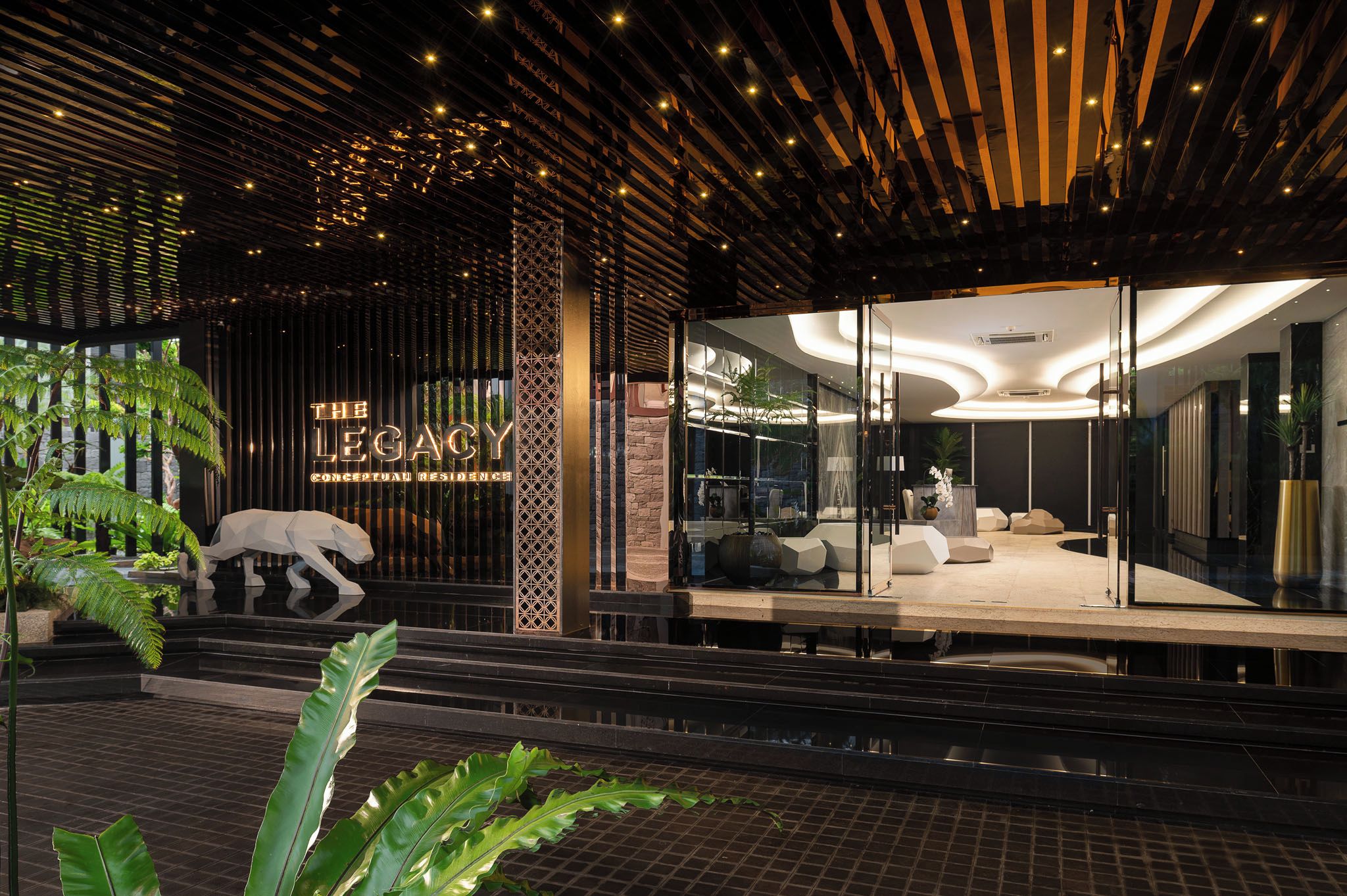 Una entrada moderna de edificio con fachada de vidrio, un cartel que dice 'The Legacy Conceptual Residence' y un área de descanso con una planta.
