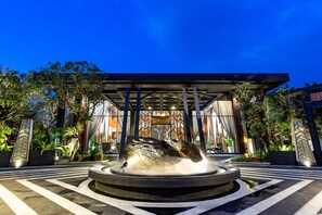 Un bâtiment moderne doté d’une fontaine centrale, entouré d’un jardin aménagé et d’un pavage décoratif.