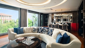 A modern living room with a curved white sofa, a coffee table, and a view of a cityscape through large windows. - The Gems Mining Pool Villas Pattaya (Pattaya)