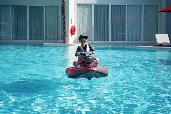Un niño sobre un jet acuático en una piscina, con un edificio al fondo.