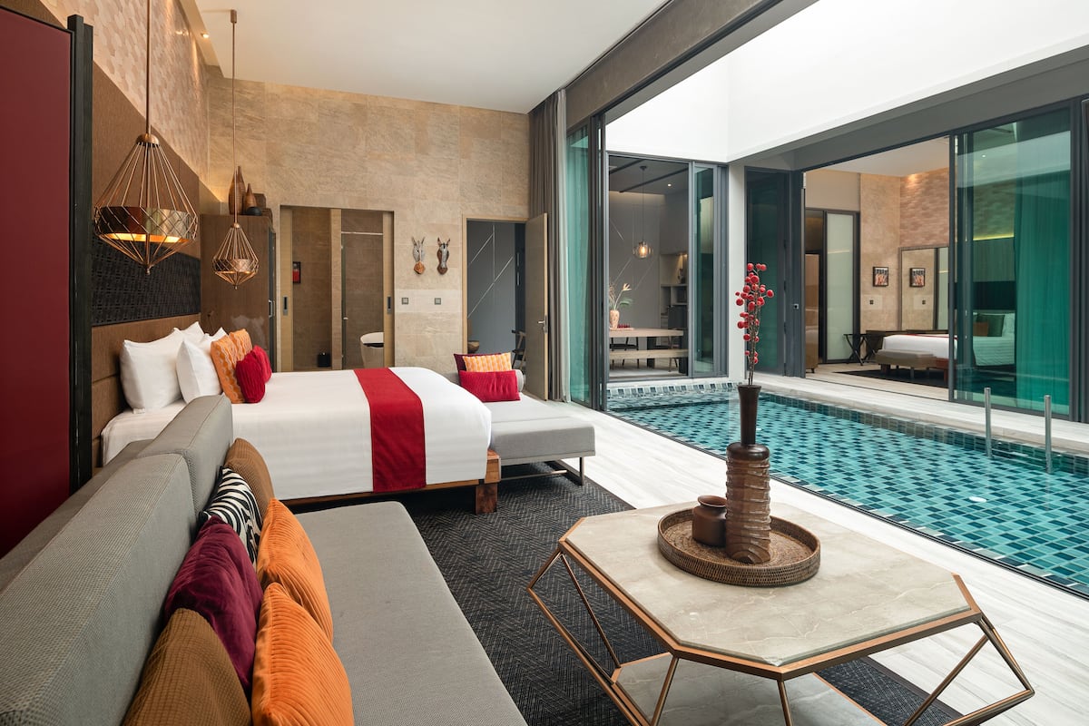 A modern hotel room with a large bed, a sofa, a small table, and a pool view.