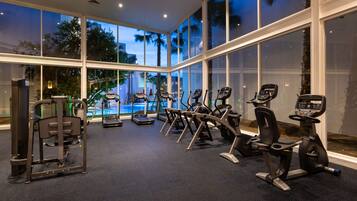 A gym with various exercise equipment, large windows, and a view of palm trees.