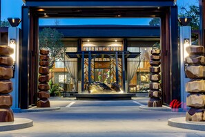 A modern building entrance with a central sculpture, large wooden pillars, and a sign that reads "Jasmine." - The Gems Mining Pool Villas Pattaya (Pattaya)