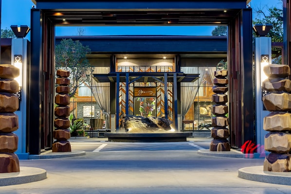 A modern building entrance with a central sculpture, large wooden pillars, and a sign that reads "Jasmine."