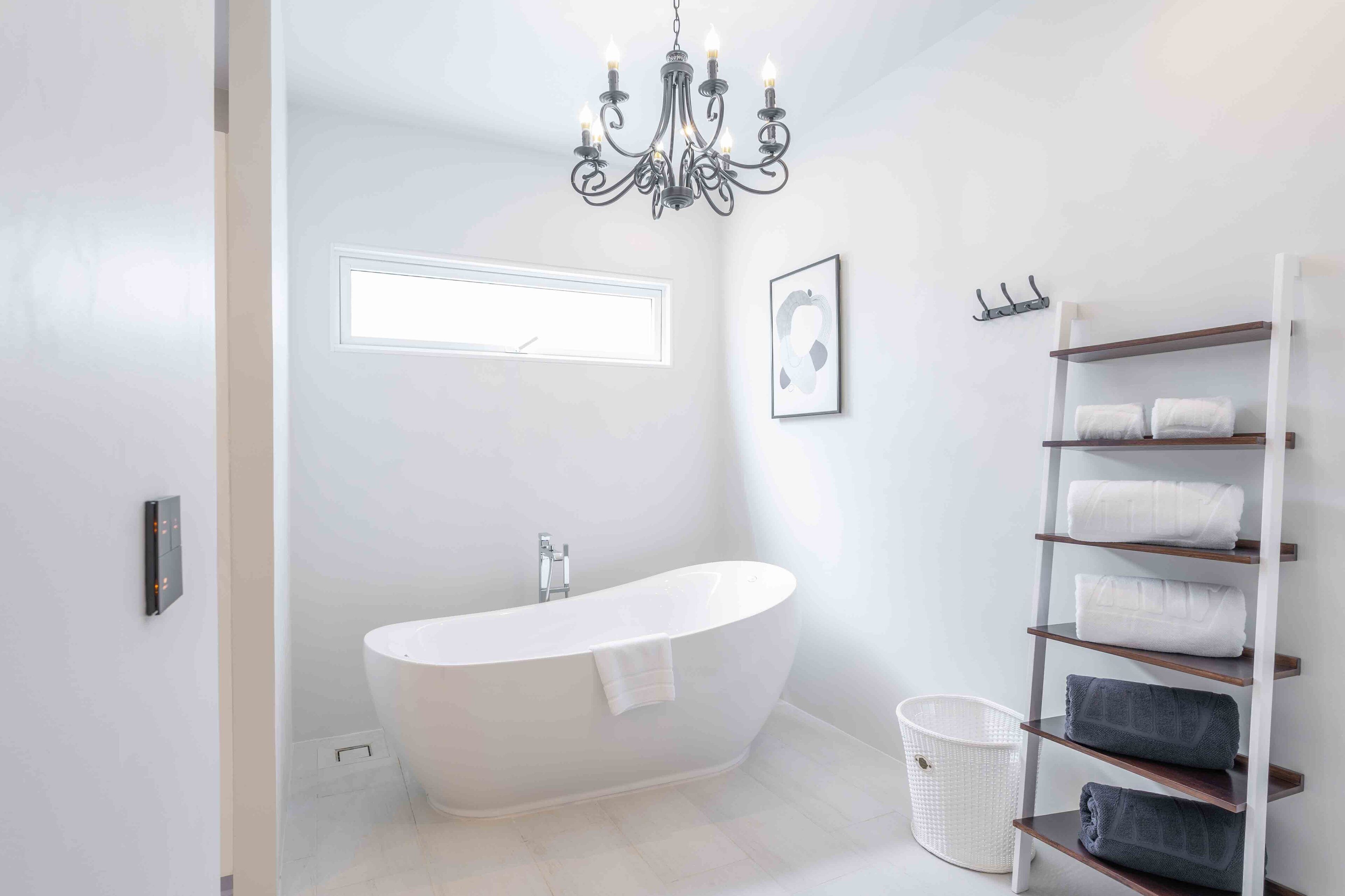 A modern bathroom with a freestanding bathtub, a chandelier, a window, a towel rack, and a built-in shelf for towels.