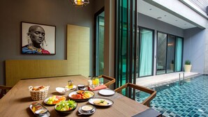 A dining table set with various dishes, a painting on the wall, and a view of a swimming pool. - The Gems Mining Pool Villas Pattaya (Pattaya)