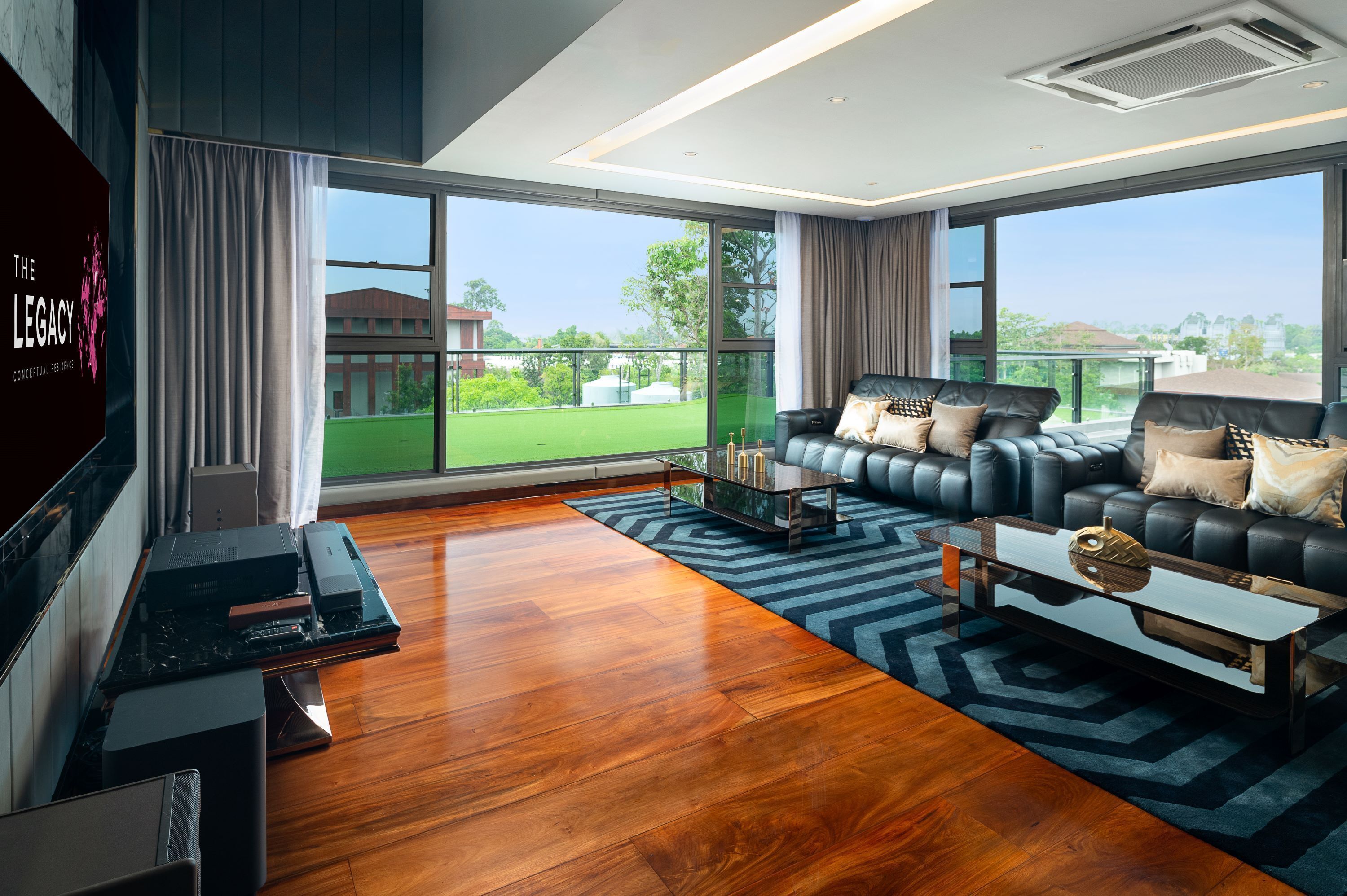 Een moderne woonkamer met een grote televisie, leren bank en uitzicht op een groen veld door grote ramen.