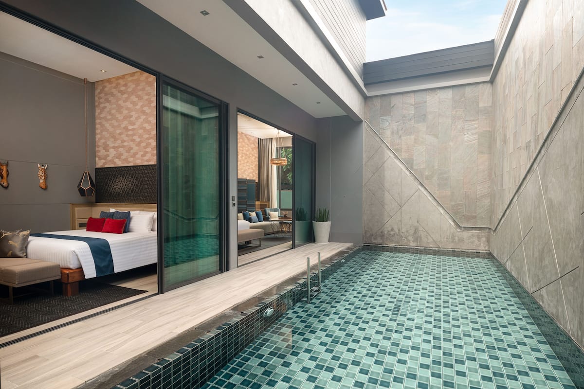 A modern hotel room with a large bed, a small seating area, and a private pool.