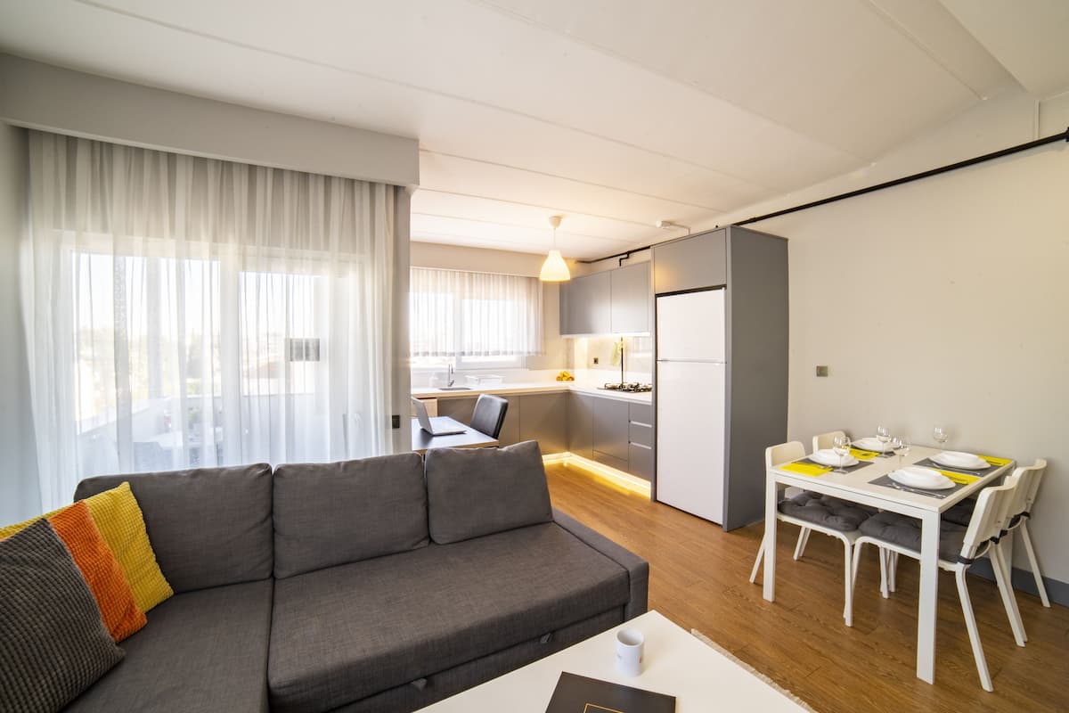 Un salon moderne avec un canapé, une table à manger dressée pour deux personnes et une cuisine en arrière-plan.