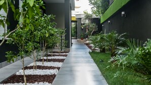 A pathway flanked by white pebbles and green plants, leading to a building with a dark facade and a green roof.