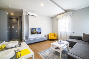 Una sala de estar moderna con comedor, un sofá, una mesa de centro y un televisor montado en la pared.
