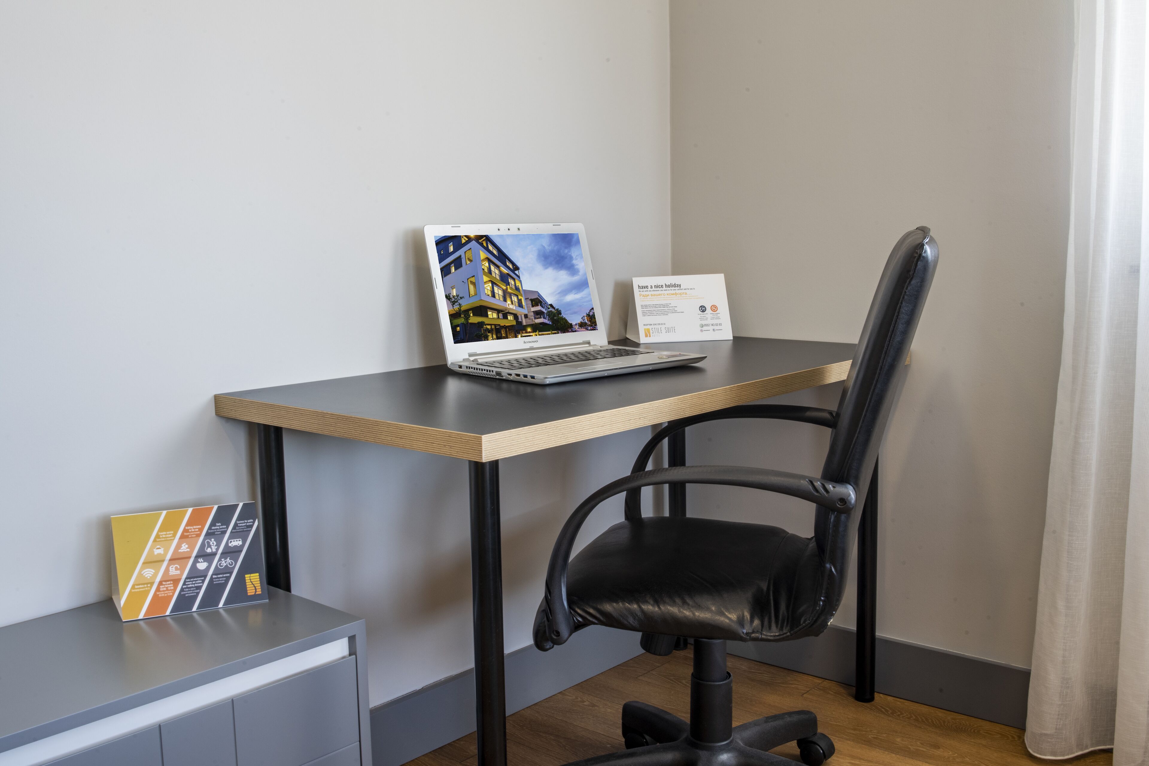 A laptop on a desk with a chair, a sign, and a small table with a folder.
