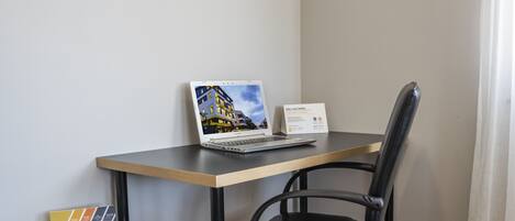 A laptop on a desk with a chair, a sign, and a small table with a folder.