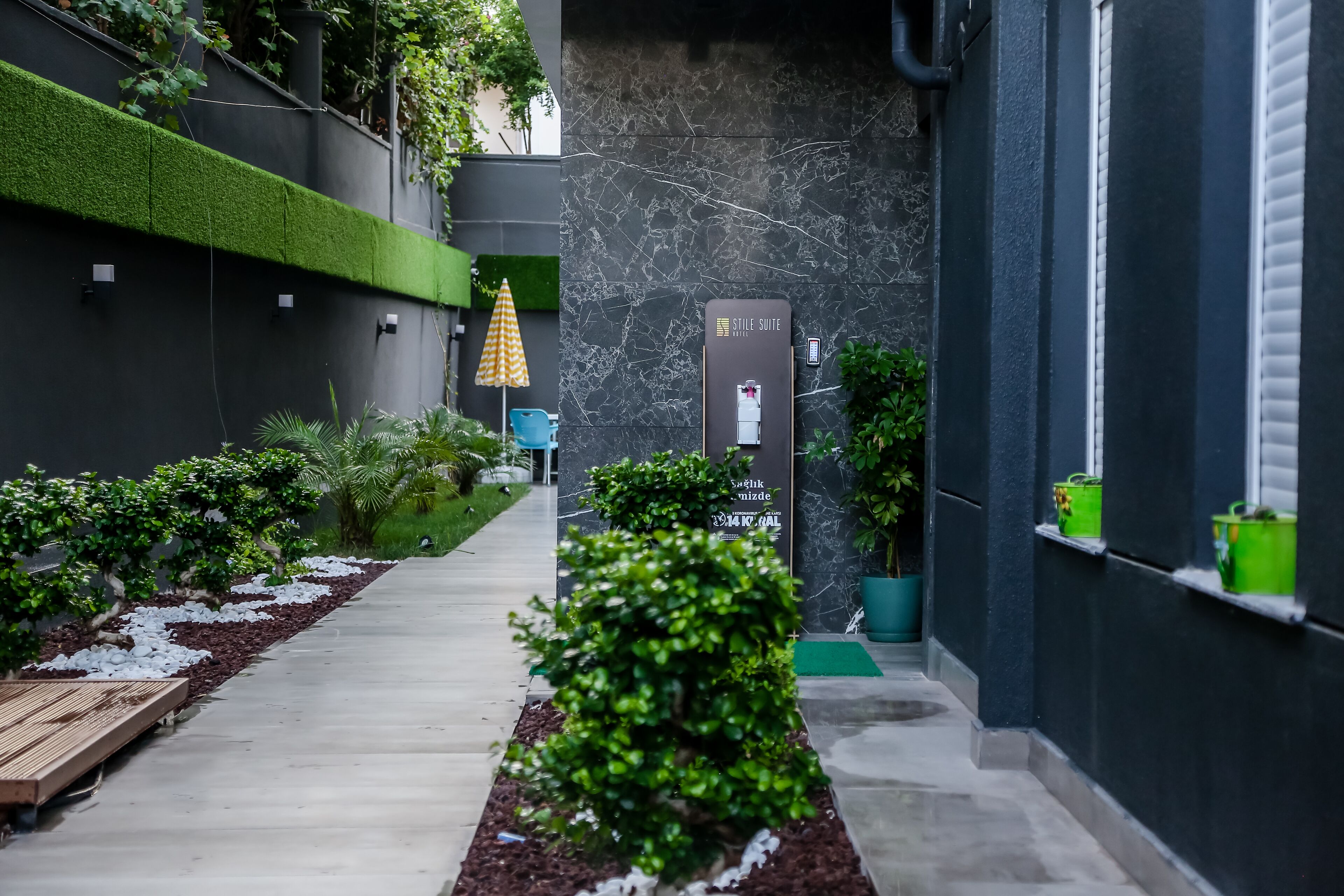 Un pasillo moderno de hotel con pared de mármol, césped artificial verde y plantas en macetas.