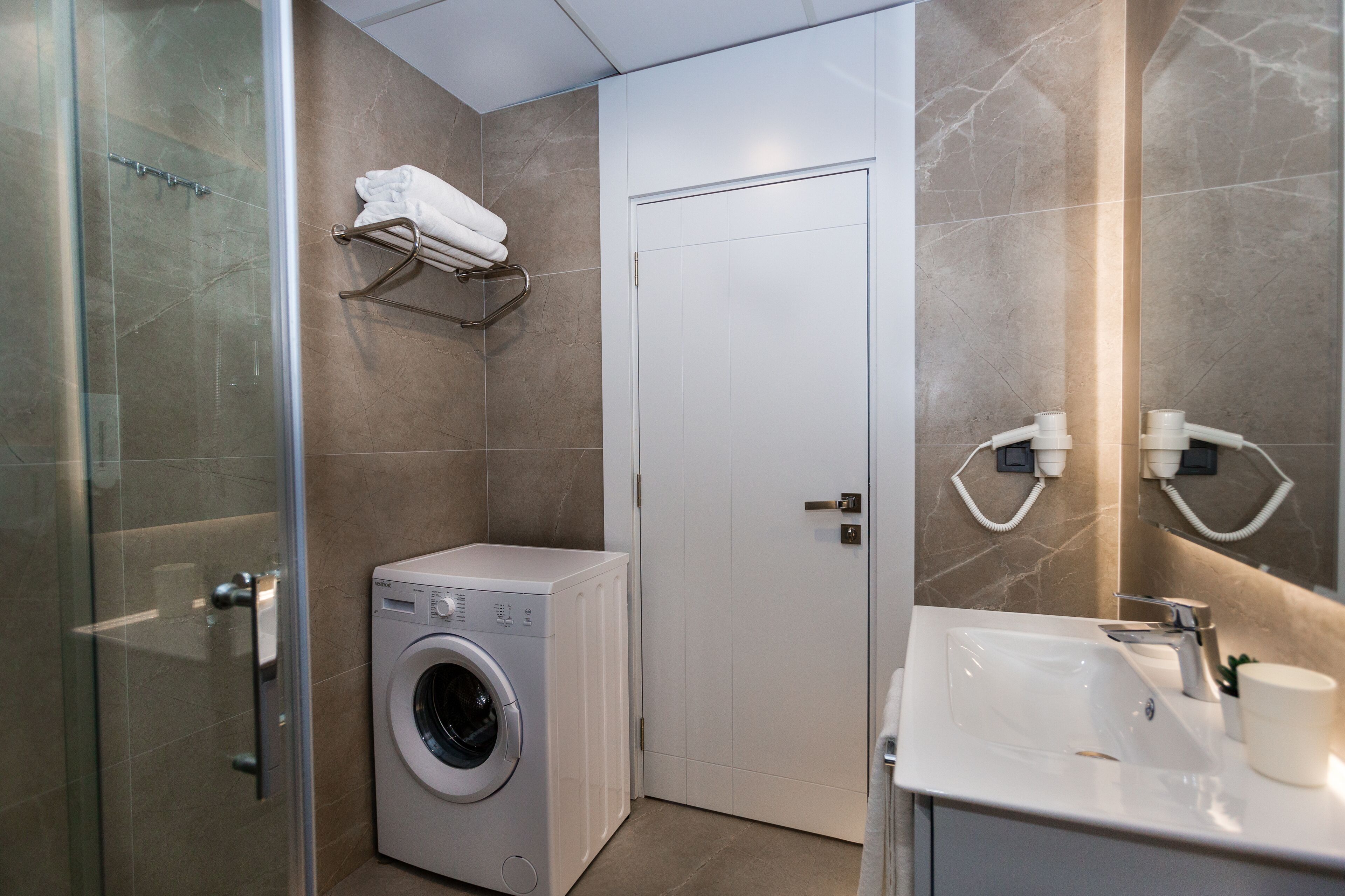 Un bagno moderno con box doccia in vetro, lavatrice integrata, lavabo bianco e porta asciugamani.