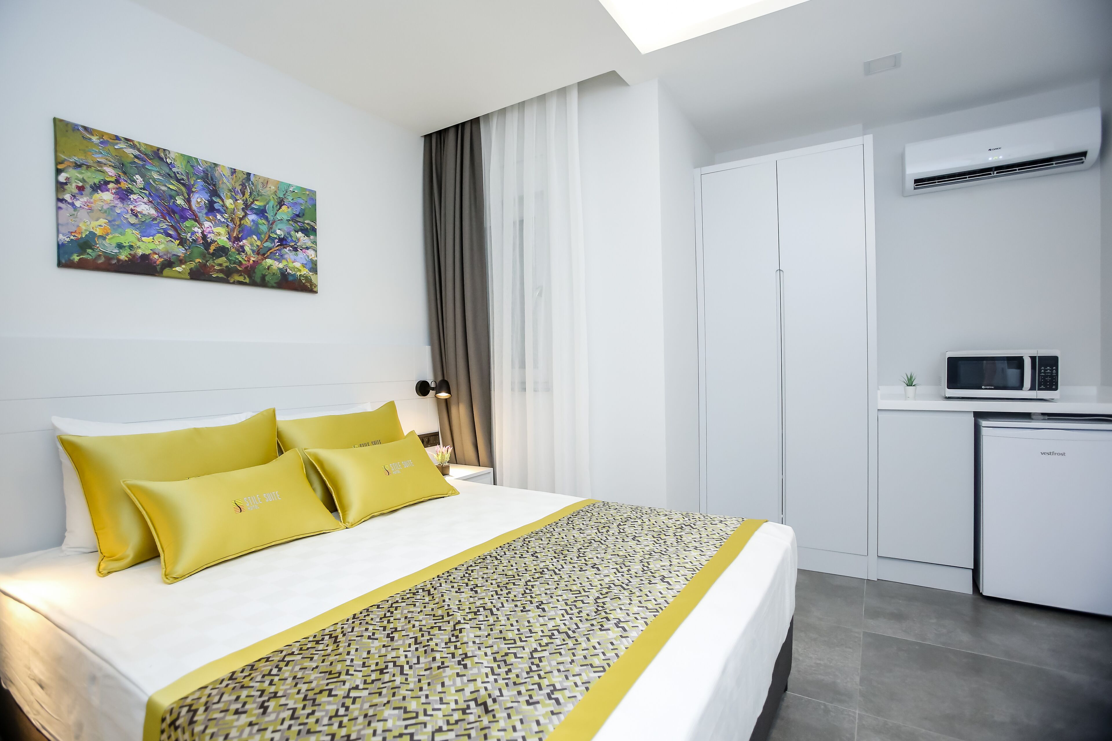A modern hotel room with a neatly made bed, a dining area, and a kitchen.