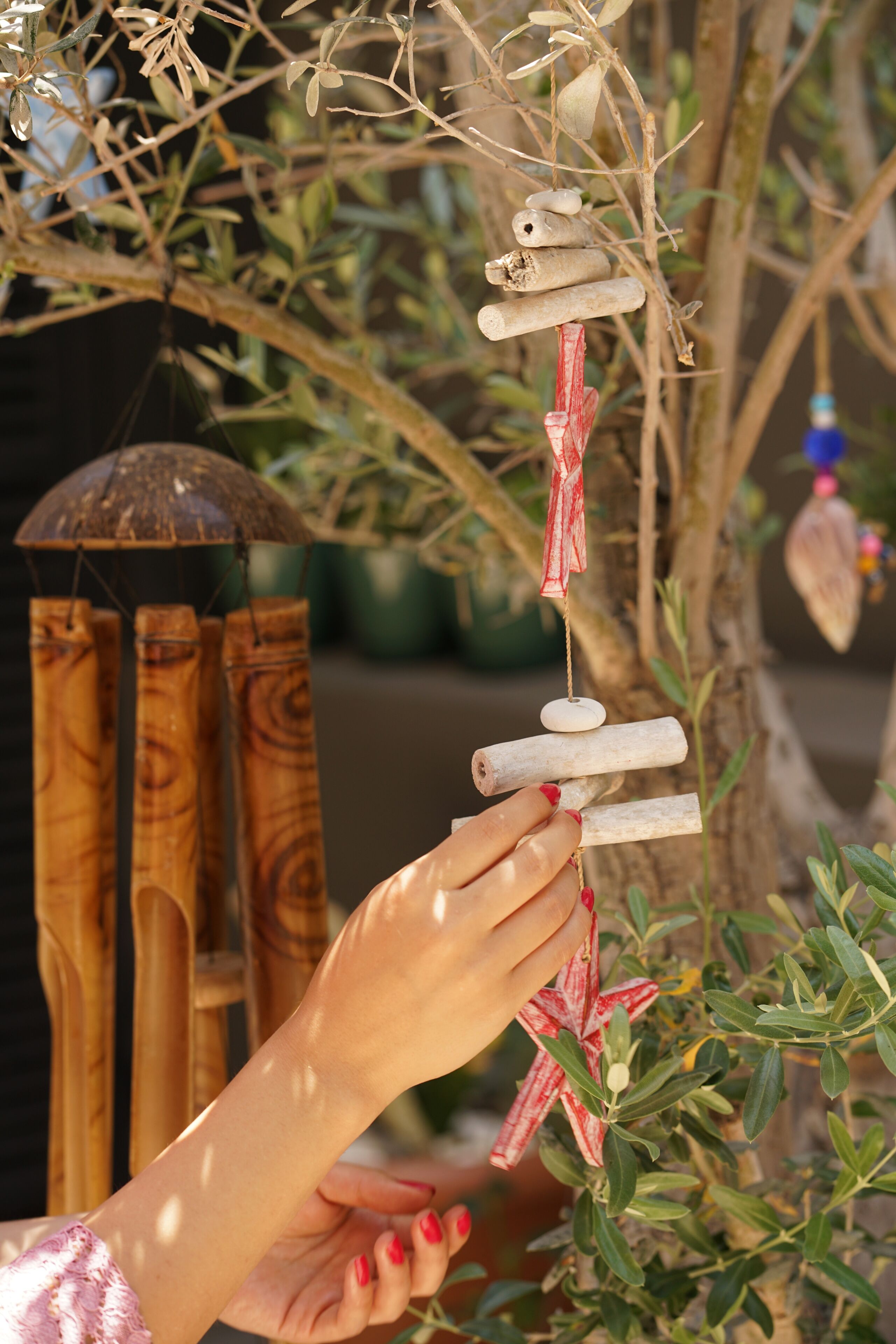 A hand holding a wind chime with wooden elements and a red ribbon.