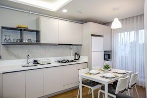 A modern kitchen with white cabinets, a marble backsplash, and a dining area with a table set for two. - Stile Suite Family Hotel (Konyaalti)