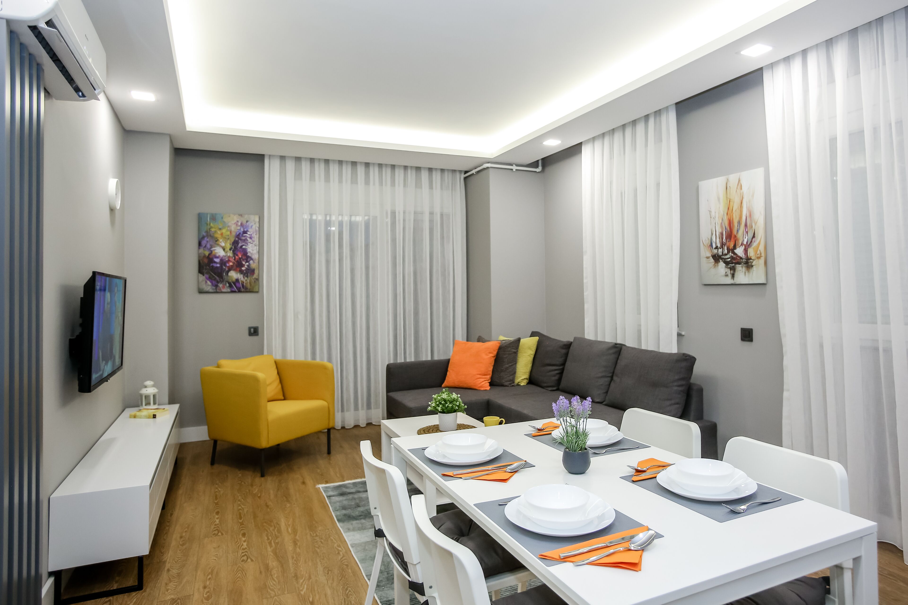 Una sala de estar moderna con zona de comedor, que incluye un sofá, un televisor y una mesa de comedor preparada para cuatro personas.