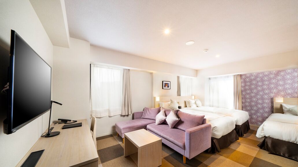 Quarto de hotel com televisão de tela plana, um sofá, duas camas, uma escrivaninha e um papel de parede estampado.
