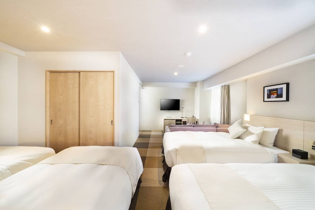 A hotel room with four beds arranged in a row, a wooden wardrobe, a television, and a desk with a chair.