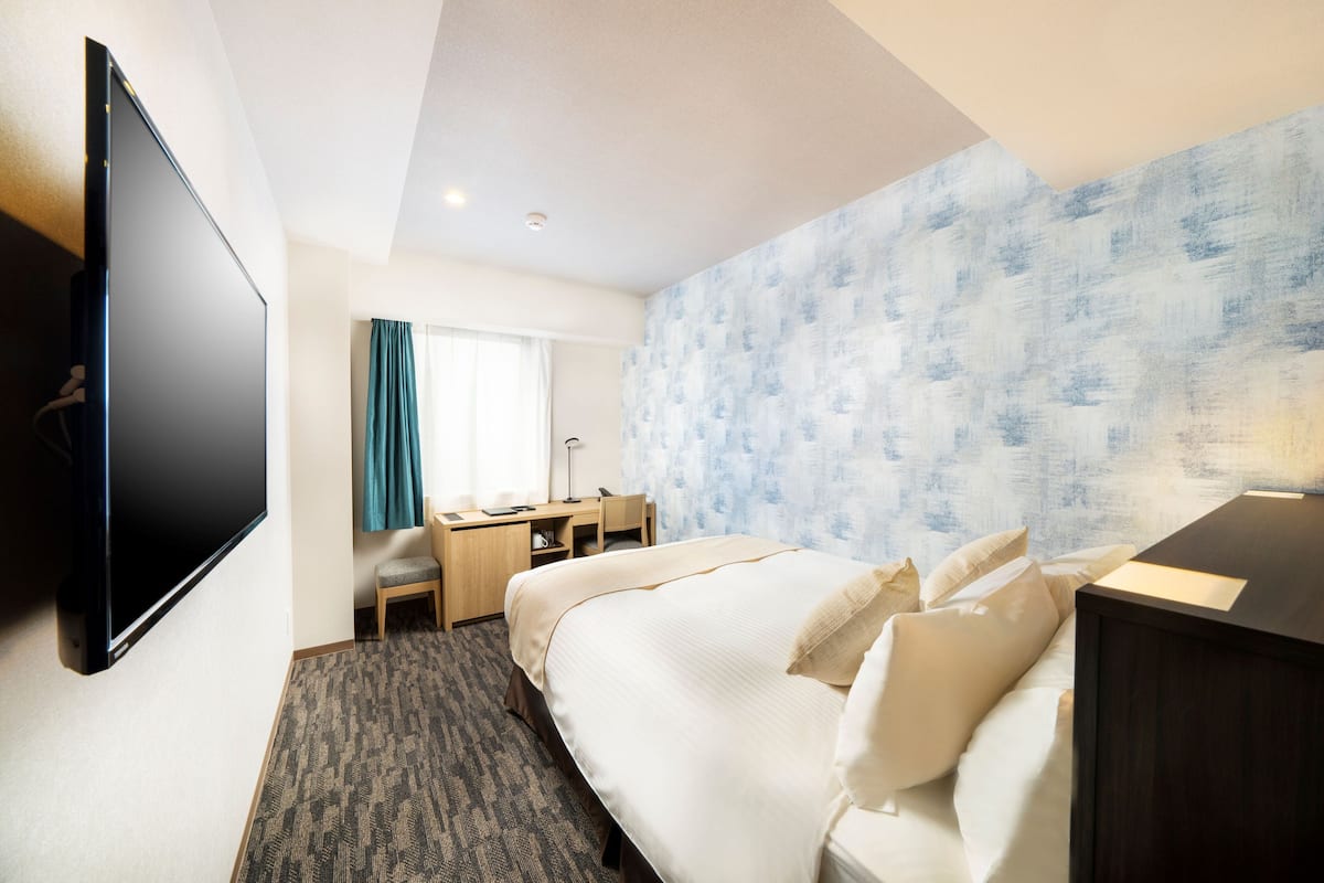 A hotel room with a bed, a desk, a chair, a TV, and a patterned wall.